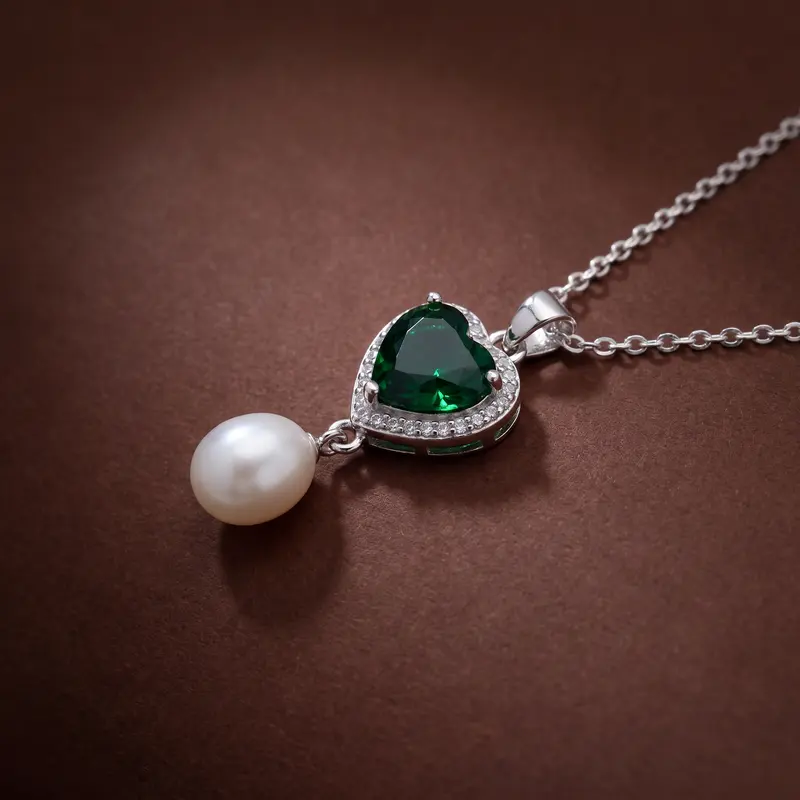 Close-up of the emerald-green heart and pearl pendant on cocoa