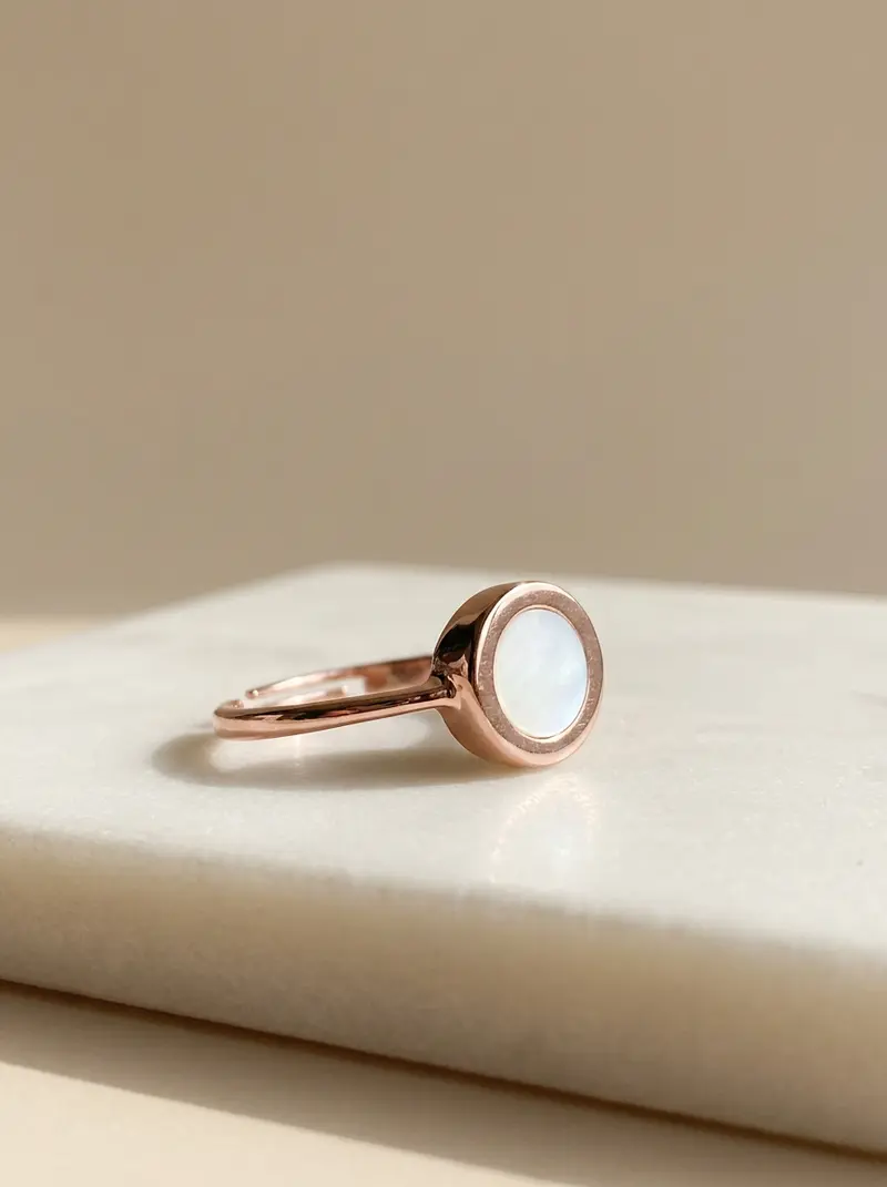 Mother-of-pearl round ring with a rose-gold finish resting on an ivory slab