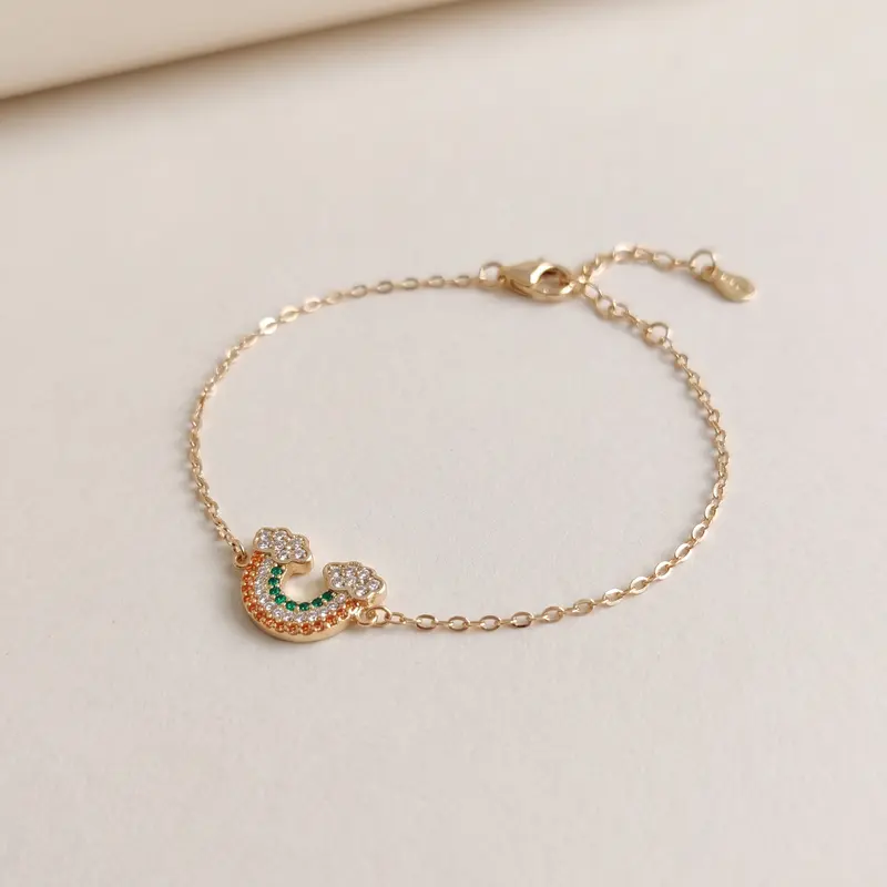 Gold-finish rainbow cloud bracelet on an off-white surface