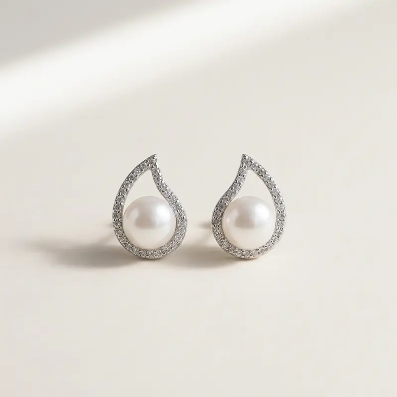 Pair of teardrop pearl studs on a warm off-white surface